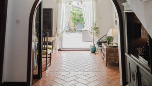 A spacious hallway with a tiled floor, a wooden staircase with ornate black railings, and a large arched doorway leading to a bright room with a view of greenery outside. - This house is a 3 bedroom(s), 3 bathrooms, located in Il-Mellieħa, null. (Il-Mellieħa)