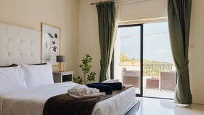 A hotel room with a bed, a nightstand, a lamp, a framed picture, a potted plant, and a balcony with a view. - This house is a 3 bedroom(s), 3 bathrooms, located in Il-Mellieħa, null. (Il-Mellieħa)