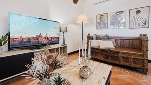 A living room with a television, a lamp, a wooden bench, and decorative items. - This house is a 3 bedroom(s), 3 bathrooms, located in Il-Mellieħa, null. (Il-Mellieħa)