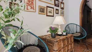 A room with a wooden chest, two wicker chairs, a table with a lamp, and various framed pictures on the wall. - This house is a 3 bedroom(s), 3 bathrooms, located in Il-Mellieħa, null. (Il-Mellieħa)