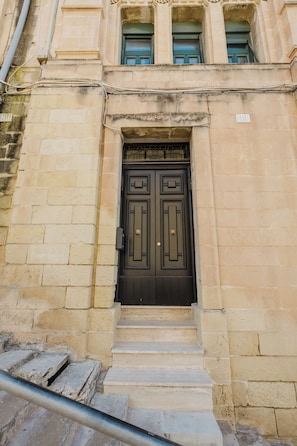 A building with a dark brown double door, stone steps leading up to it, and a window with green shutters above. - Historic maisonette Malta, Balluta Bay seafront apartment, heritage apartment Malta, St Julian’s maisonette, Balluta Buildings stay, authentic Malta accommodation. (St. Julian's)