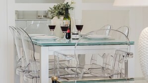 Un coin repas avec une table et des chaises en verre, un vase rempli de fleurs et des verres à vin.