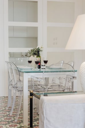 A dining area with a glass table and chairs, a vase with flowers, and wine glasses.