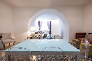 Uma sala de estar moderna com uma mesa de jantar de vidro, cadeiras transparentes, um sofá e um tapete estampado.