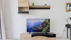 A modern living room with a flat-screen TV mounted on a wooden stand, a small wooden shelf above it, and a round wooden coffee table in the center.