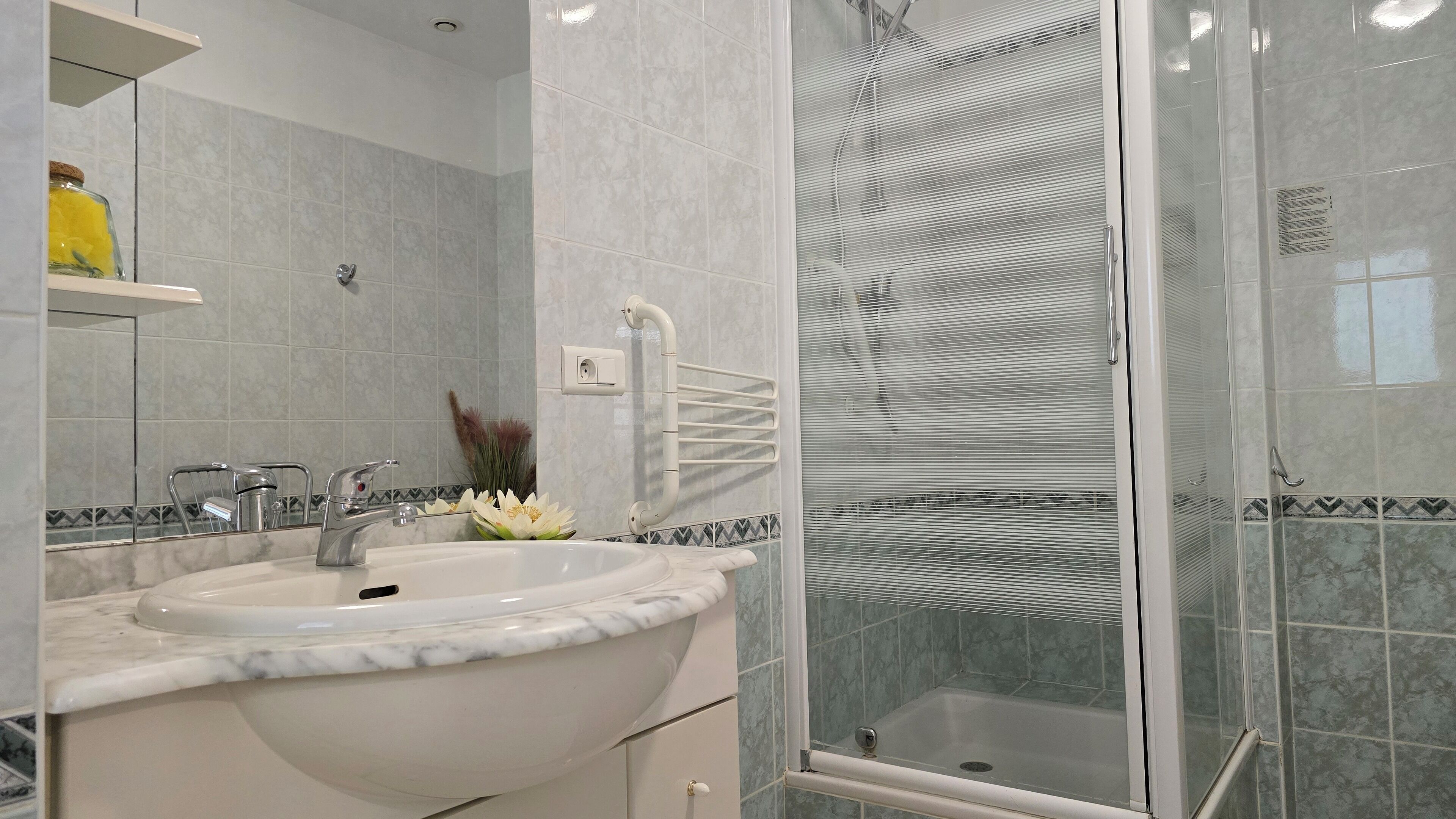 A bathroom with a marble sink, a glass shower enclosure, and a mirror.