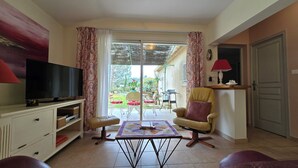 Un salon comprenant un téléviseur, un canapé, un fauteuil, une table avec une courtepointe et une porte-fenêtre coulissante donnant sur un espace extérieur.