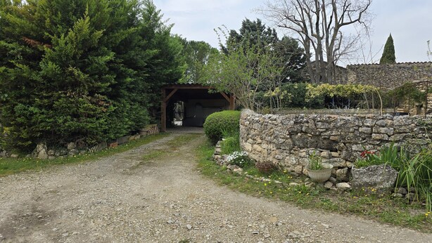 Un chemin de gravier mène à un bâtiment aux murs de pierre, surmonté d’une arche en bois.