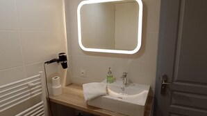 Een badkamer met een witte wastafel, een spiegel met verlichting en een handdoekhouder.