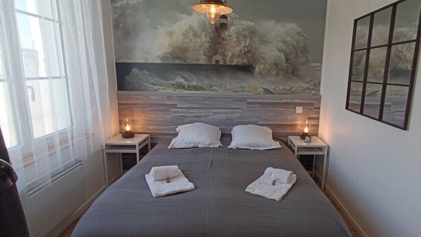 Een slaapkamer met een bed, twee nachtkastjes met lampen, een groot raam en een muurschildering.