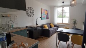A modern kitchen with a dining area, a sofa, and a large window. - Superb T1 of 28 M2 (CAEN)