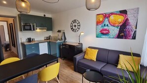 A modern living room with a sofa, a dining table, and chairs. There is a kitchen area with cabinets and a microwave. A clock is on the wall. - Superb T1 of 28 M2 (CAEN)