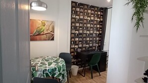 Ein kleiner, gut beleuchteter Raum mit einem Esstisch, Stühlen, einer Zimmerpflanze und einer Wand mit gerahmten Bildern.