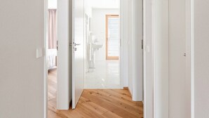 A hallway with wooden flooring and white walls, leading to a room with a glass door and a bathroom visible through it. - Marllon Suites – Verso Apartment (Lörrach)