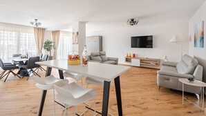 A modern living room with a dining area, a sofa, a TV, and a lamp. - Marllon Suites – Verso Apartment (Lörrach)
