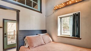 A bedroom with a bed, a window with curtains, a light fixture, and a door. - Modern mountain bungalow with private patio + epic Mt. Princeton views (Buena Vista)