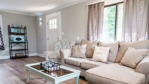 A living room with a beige sofa, a patterned armchair, a coffee table, and a bookshelf with vintage radios. - In town with a view, private duplex. (Bryson City)
