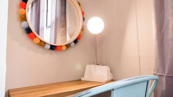 Une salle de bain avec un meuble-lavabo en bois, un miroir rond orné de pompons colorés et une lampe blanche à abat-jour rond.