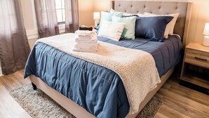 A neatly made bed with a blue and white duvet, a stack of folded towels, and a variety of pillows. - In town with a view, private duplex. (Bryson City)