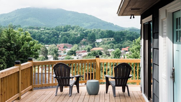A wooden deck with two chairs and a table, overlooking a mountainous landscape with buildings. - In town with a view, private duplex. (Bryson City)