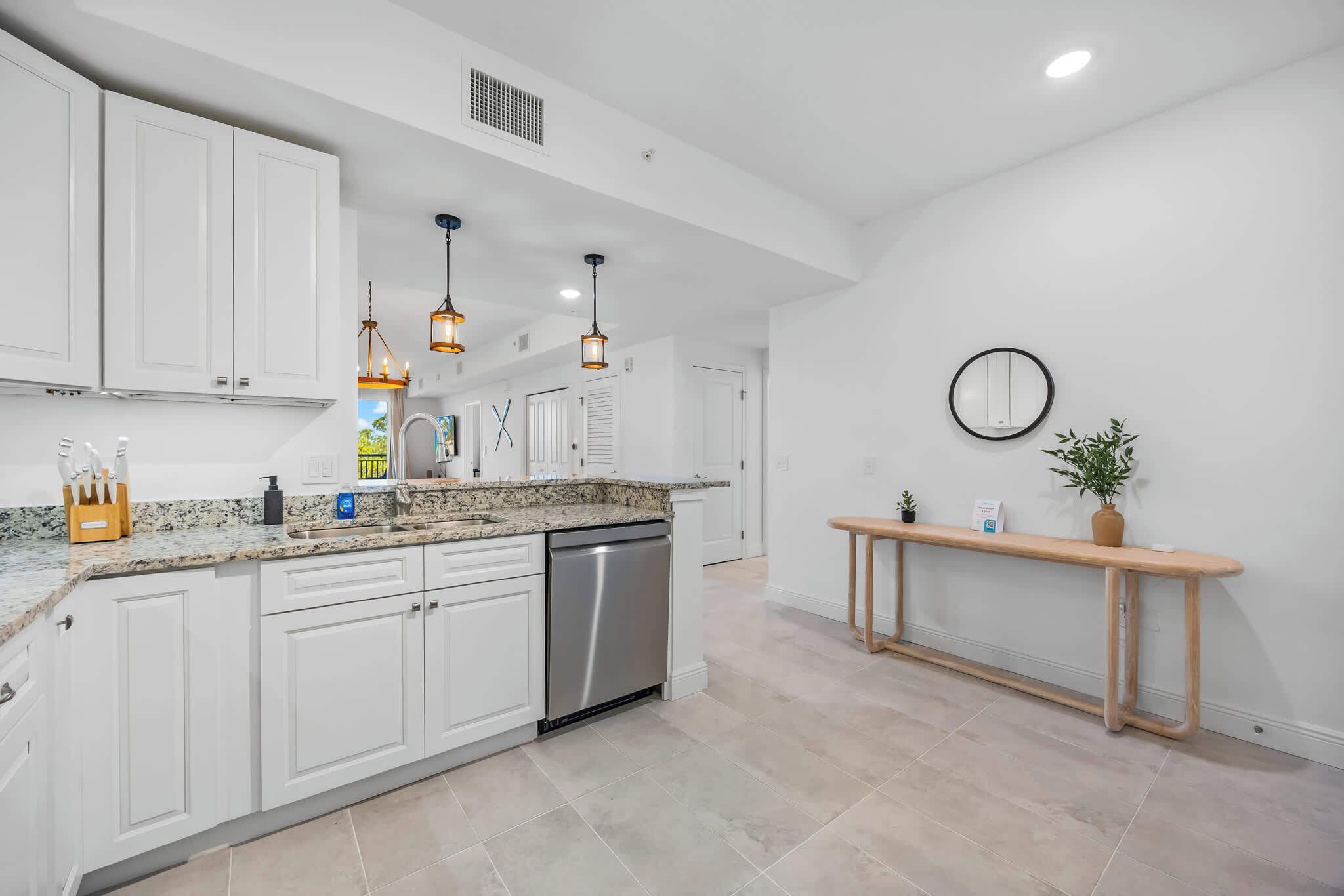 A modern kitchen with white cabinets, a stainless steel dishwasher, and pendant lighting.