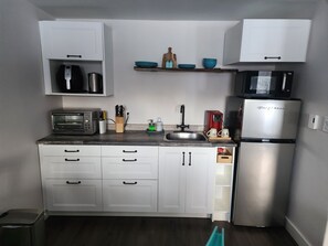 Uma cozinha moderna com armários brancos, geladeira de aço inoxidável, micro-ondas, torradeira e pia.