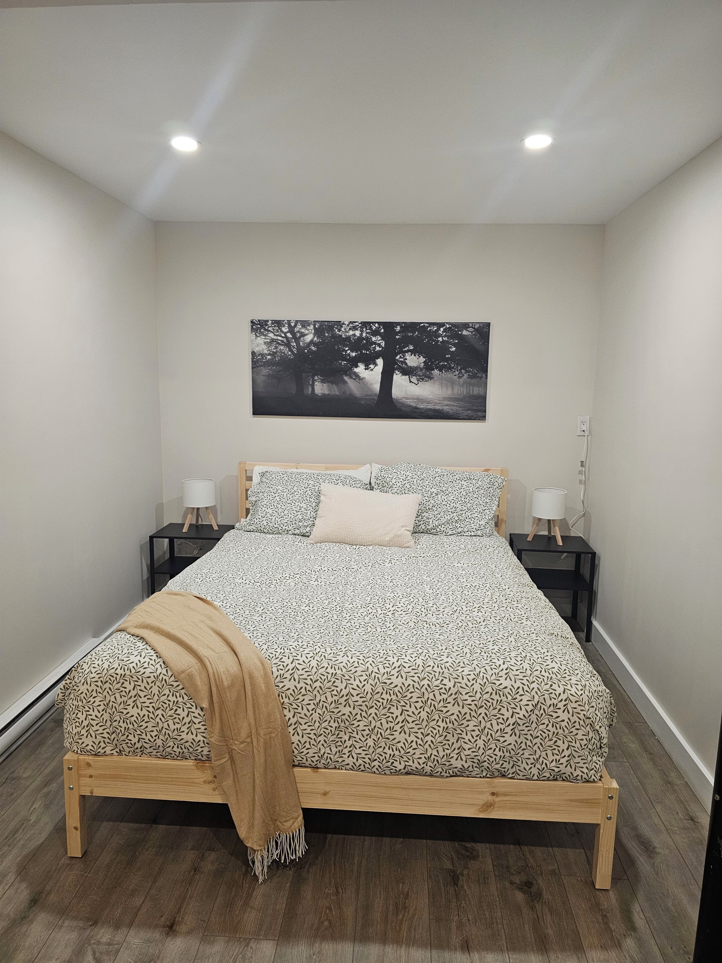 Une chambre à coucher avec un lit, deux tables de chevet, une commode, un tableau accroché au mur et un plancher en bois.