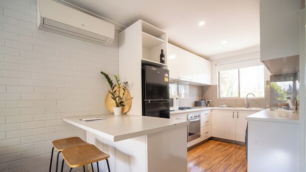 Cozinha moderna com armários brancos, uma ilha central com banquetas, geladeira preta e uma janela que oferece luz natural.