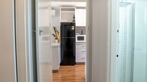 Um corredor com piso de madeira que leva a uma área de cozinha com armários brancos e uma geladeira preta.
