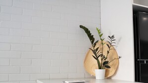 Uma cozinha moderna com bancada branca, dois bancos de madeira, uma planta em vaso e uma geladeira preta.