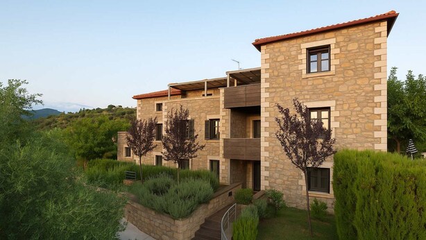 Un edificio de varios pisos de piedra con balcones, rodeado de abundante vegetación y un cielo despejado.