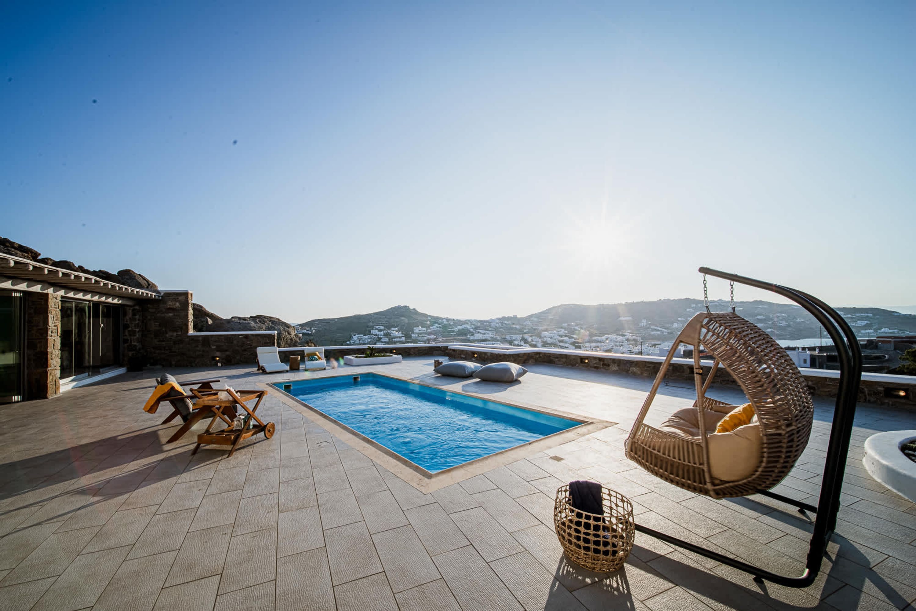 A rooftop pool area with a swing chair, lounge chairs, and a view of the landscape.