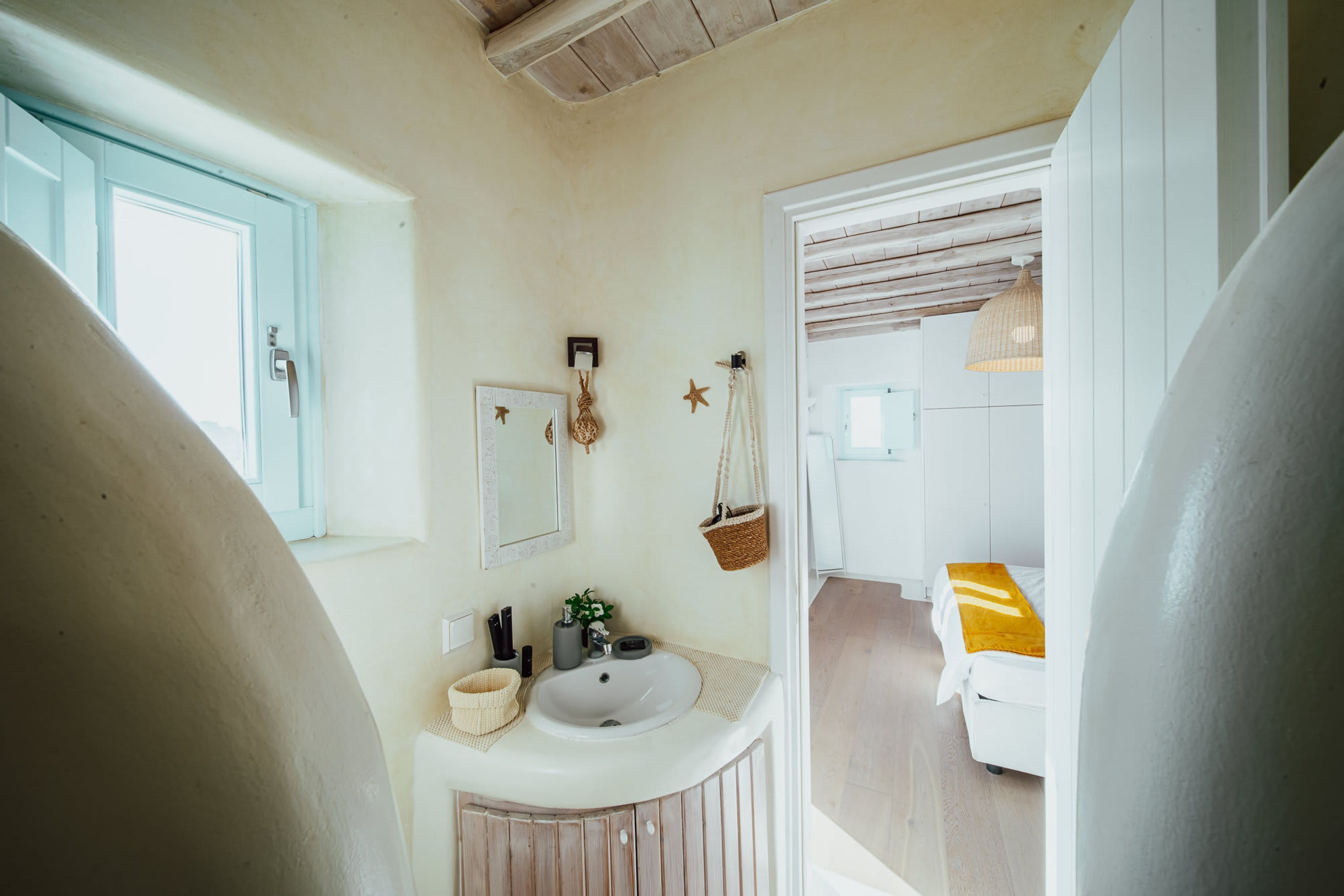 Un baño con lavamanos blanco, tocador de madera y una cesta colgante.