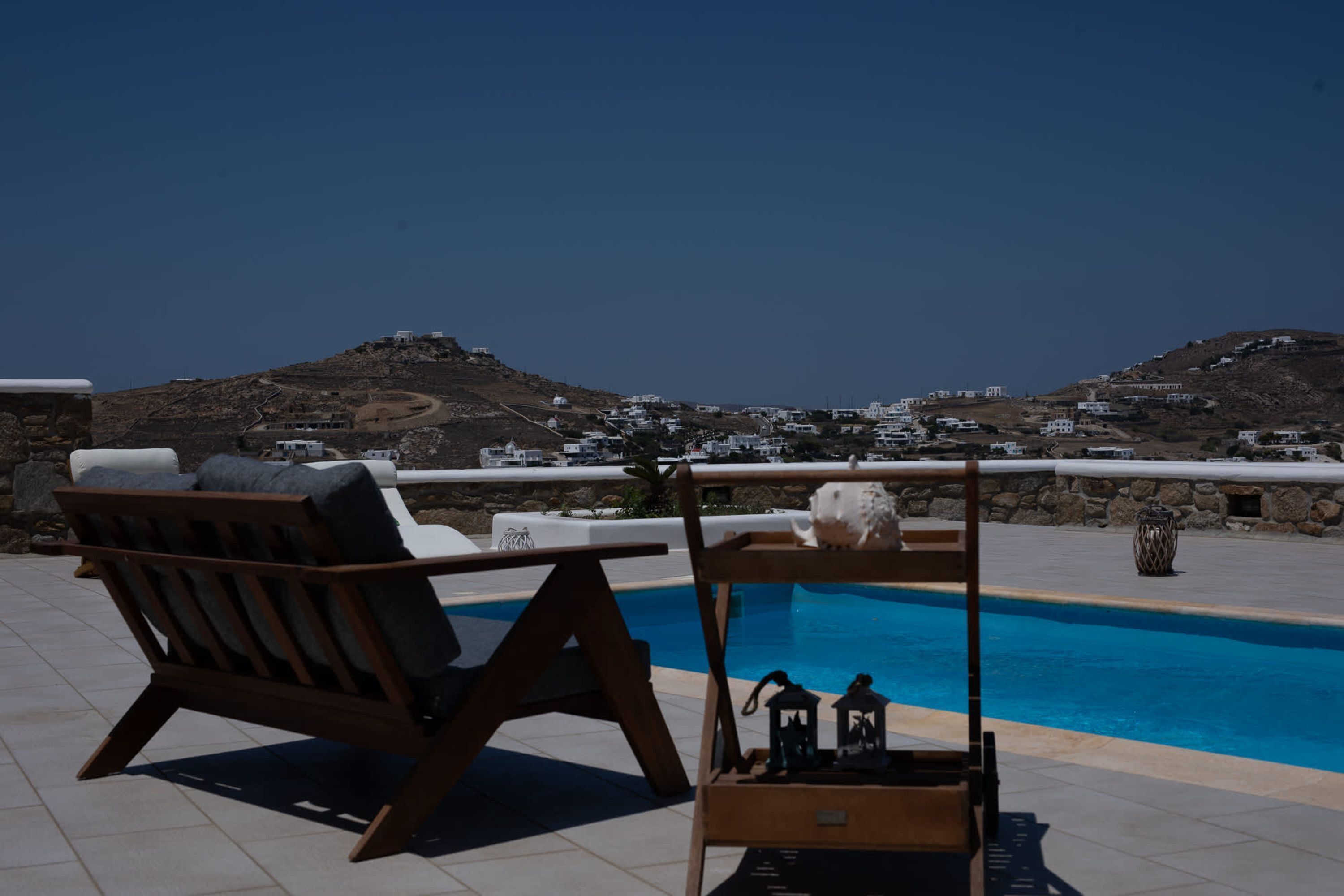 A poolside area with a wooden lounge chair and a small table with decorative items.