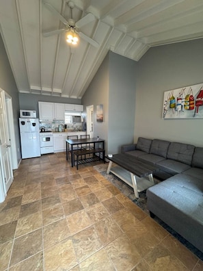 A spacious living area with a gray sofa, a dining table, and a kitchen in the background. - Charming 2BR Beach Condo with Parking (Point Pleasant Beach)