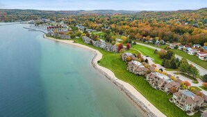 Un quartier résidentiel situé sur la côte, avec des maisons le long du littoral, un port de plaisance et, en arrière-plan, des arbres aux couleurs automnales.