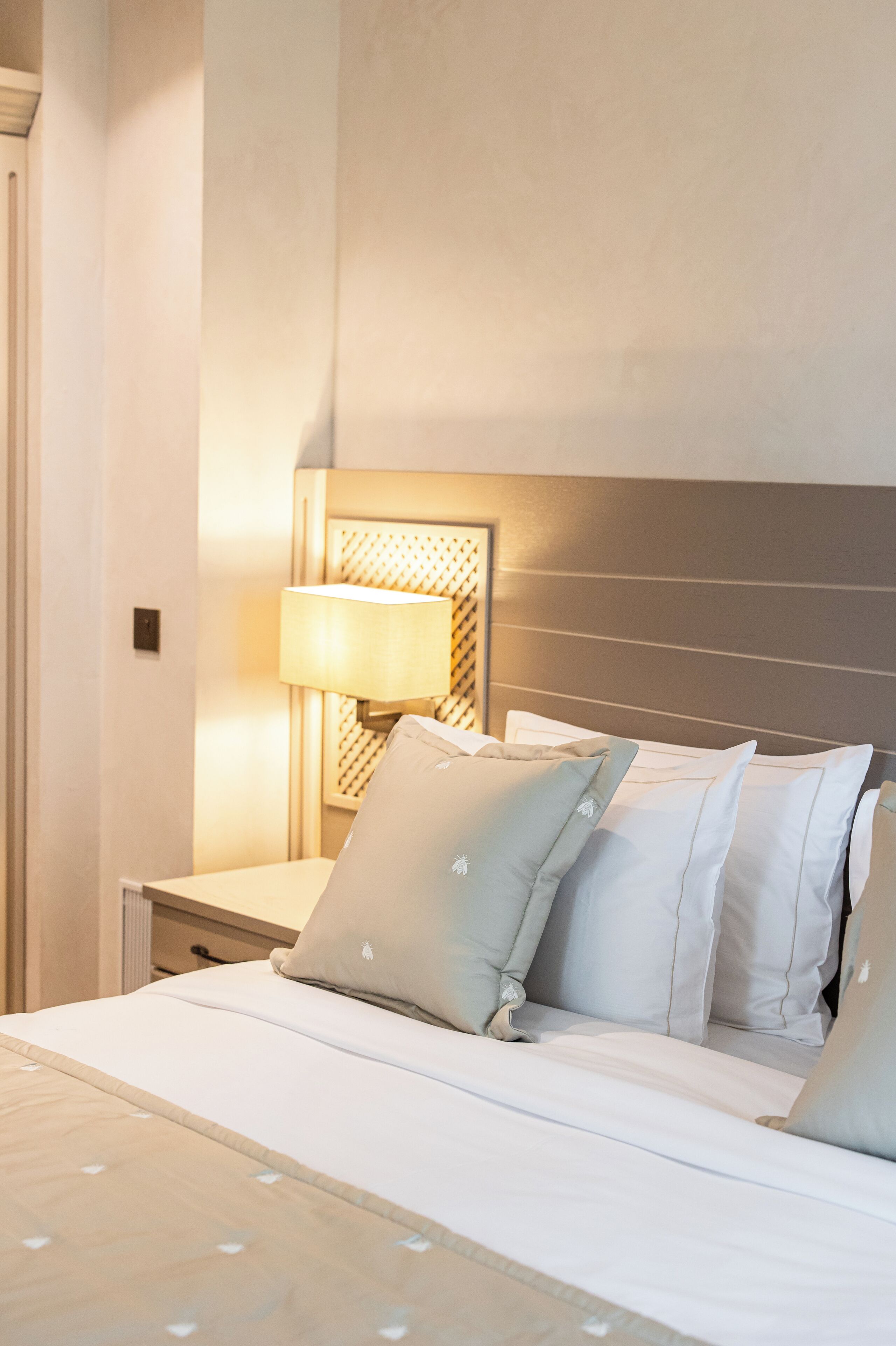 A neatly made bed with white bedding and light blue pillows, a bedside lamp, and a headboard with a textured design.
