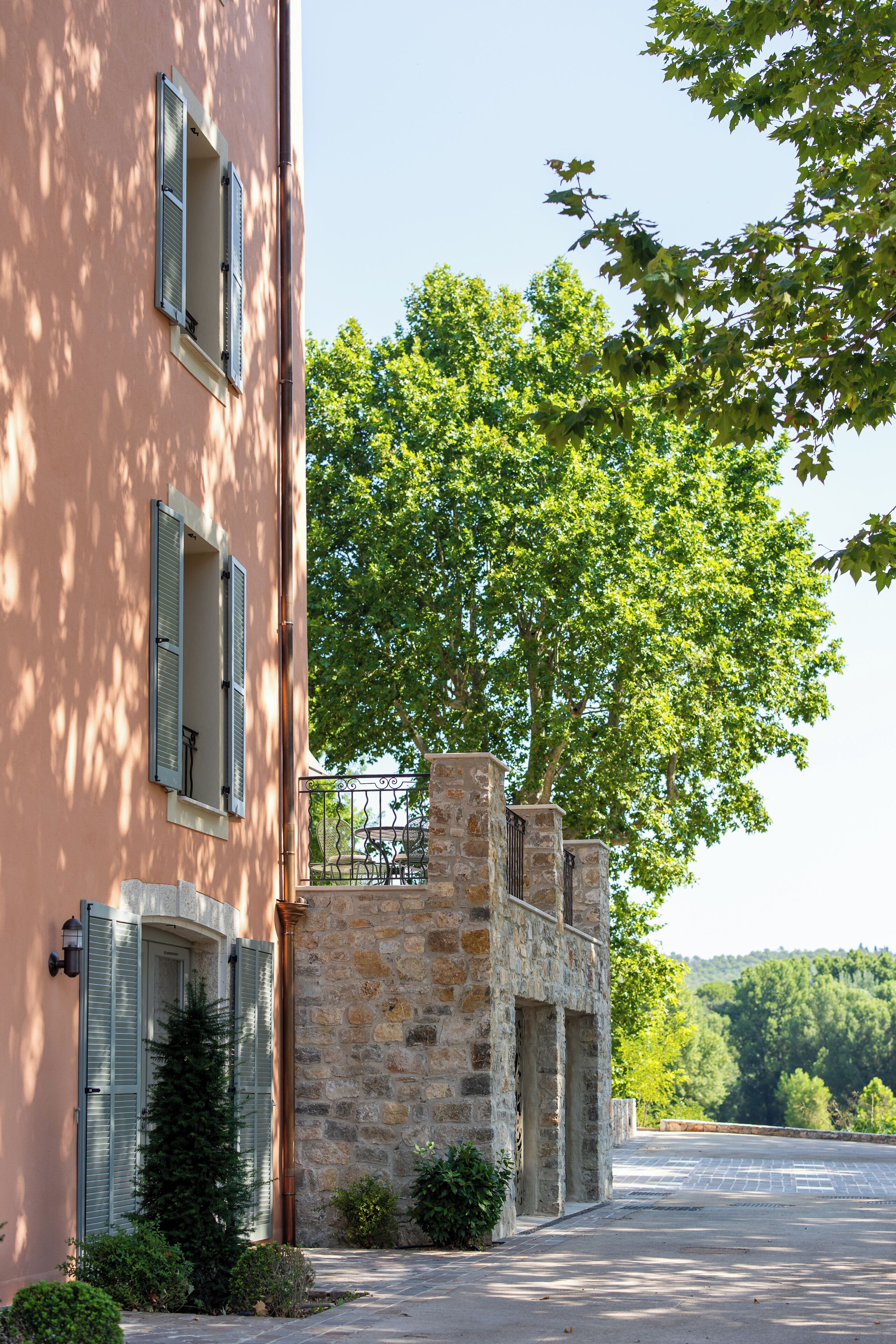Un edificio de fachada de piedra, un árbol en primer plano y un área pavimentada.