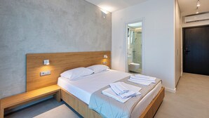 A modern hotel room with a wooden bed, bedside tables, a large mirror, and a door leading to a bathroom. - Lucciola Boutique Rooms (Budva)