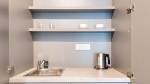 A modern kitchen with a stainless steel sink, a kettle, and white shelves above the countertop. - Lucciola Boutique Rooms (Budva)