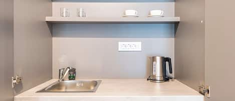Una cocina moderna con un lavamanos de acero inoxidable, una tetera y estantes blancos sobre la encimera.