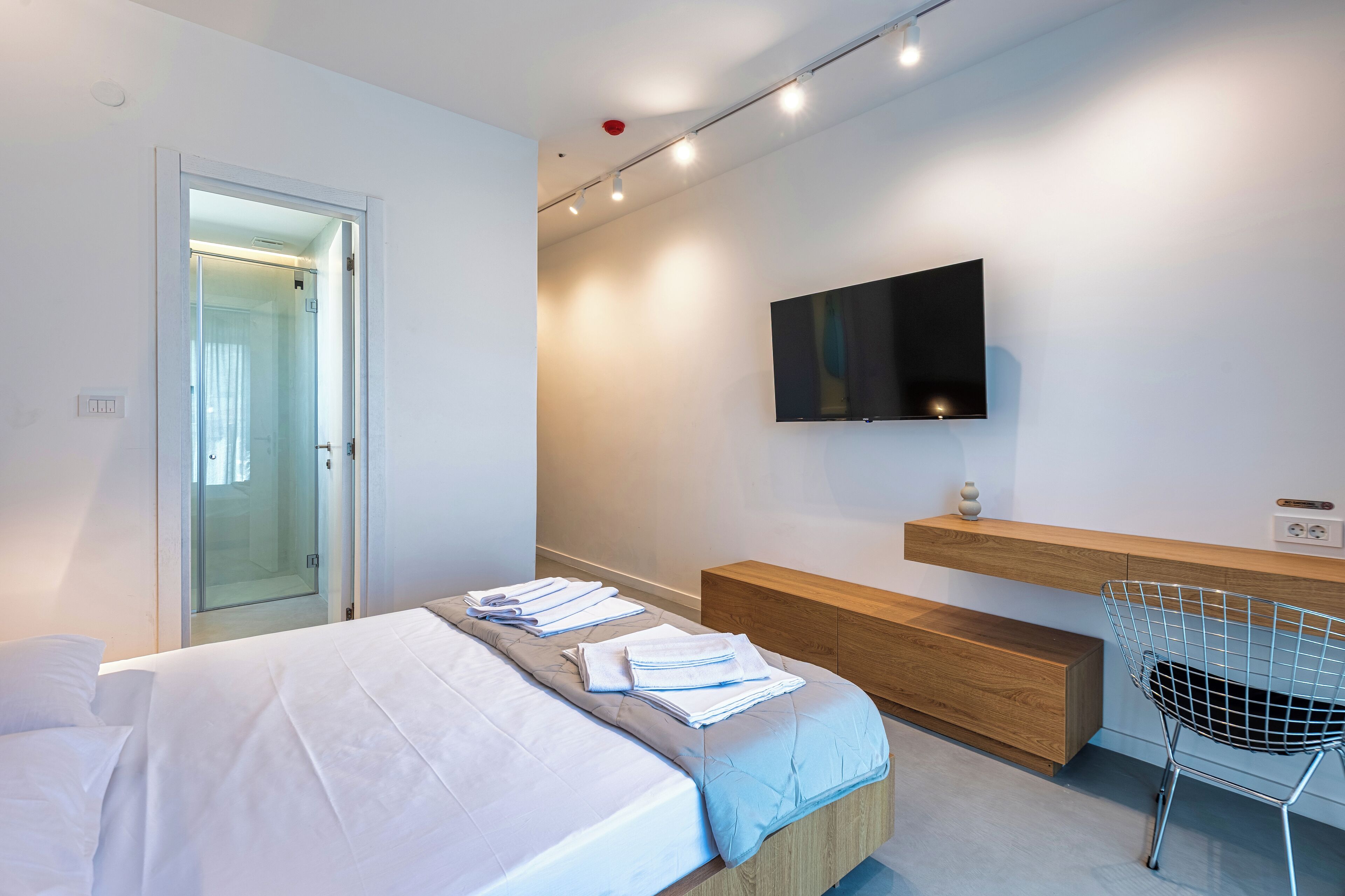 Una habitación de hotel moderna con una cama, un televisor montado en la pared, un banco de madera y una silla.