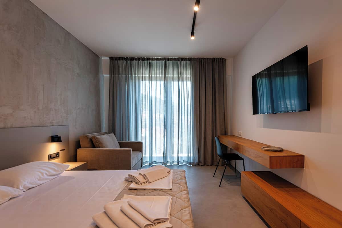 A modern hotel room with a large bed, a desk, a chair, and a TV mounted on the wall.
