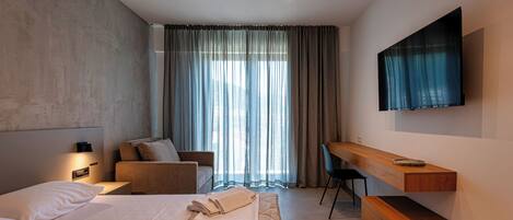 A modern hotel room with a large bed, a desk, a chair, and a TV mounted on the wall.
