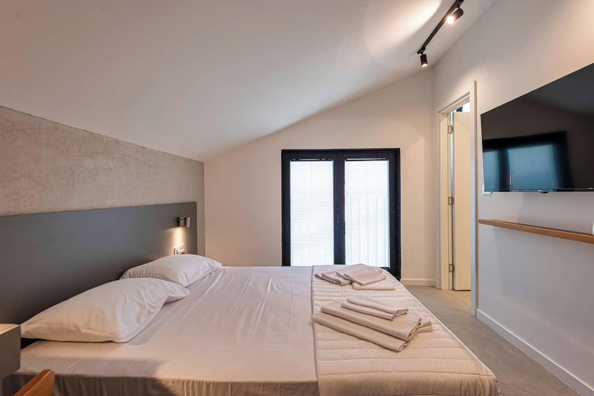 A modern bedroom with a large bed, a TV mounted on the wall, and a door leading to another room.