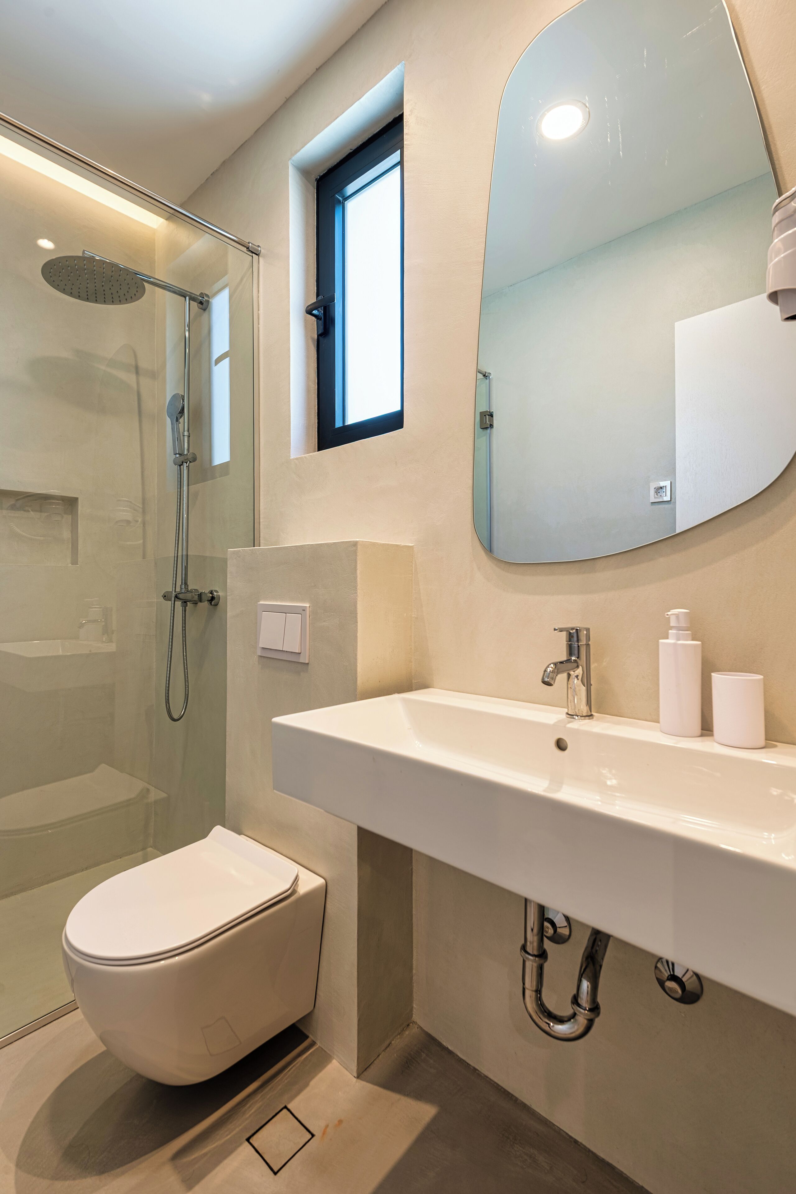 Un baño moderno con ducha de vidrio, inodoro blanco, espejo grande y lavamanos blanco con grifo.