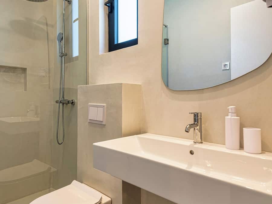 Un baño moderno con ducha de vidrio, inodoro blanco, espejo grande y lavamanos blanco con grifo.