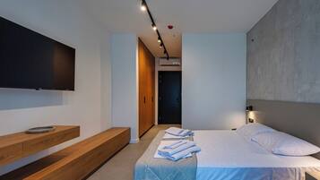 Une chambre d’hôtel moderne équipée d’un lit, d’un banc en bois, d’un téléviseur à écran plat et d’un luminaire fixé au mur.