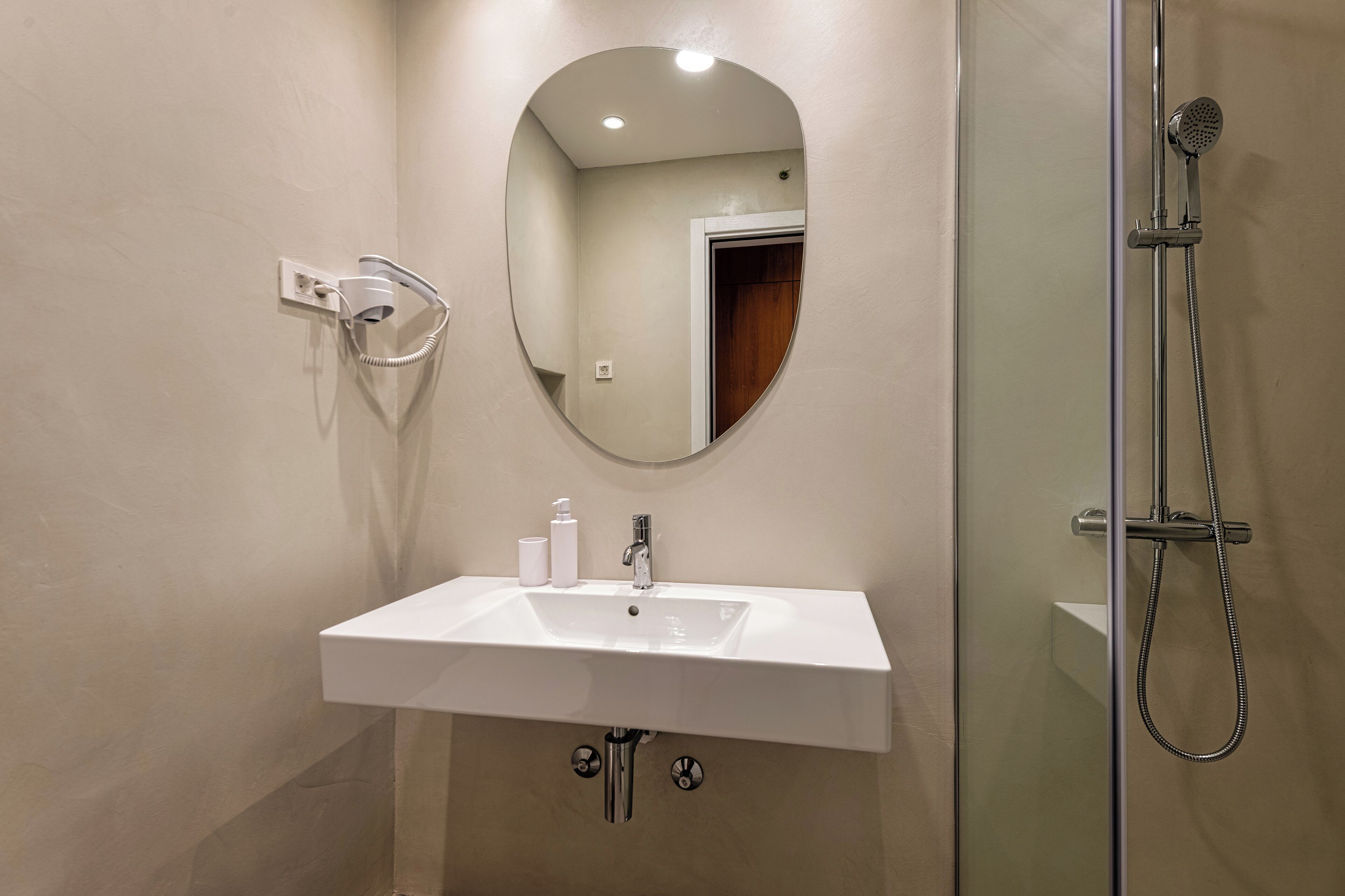 A bathroom with a white sink, a mirror, a handheld showerhead, and a glass-enclosed shower.