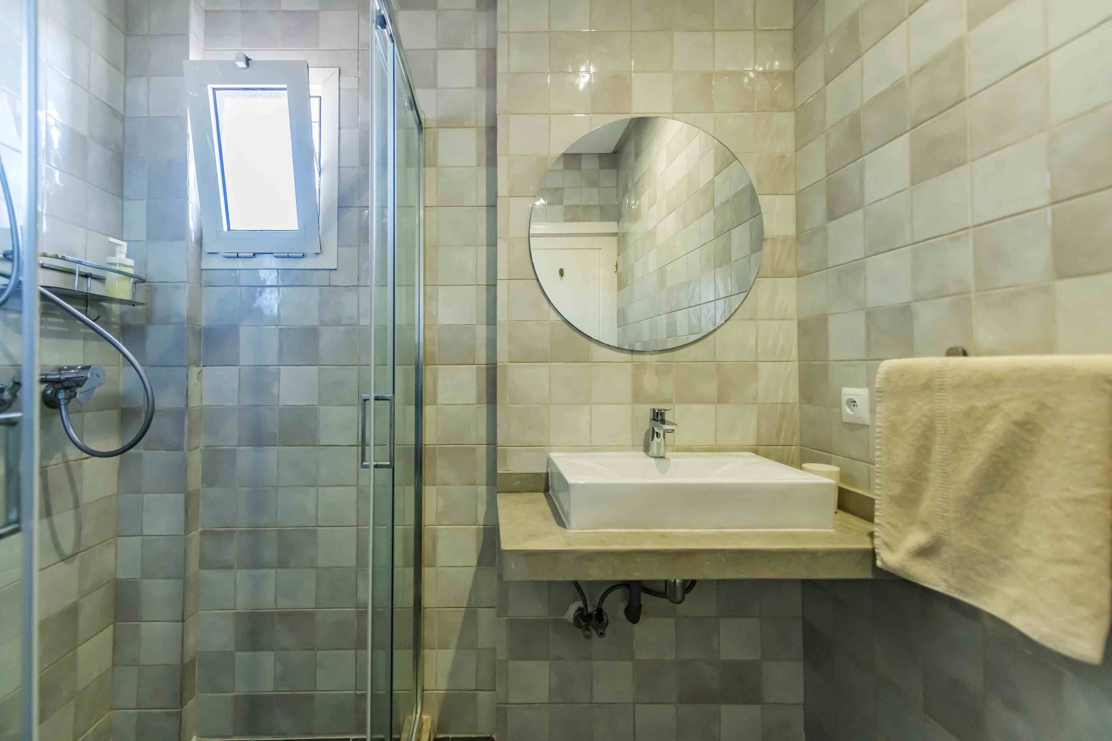 A bathroom with a glass shower enclosure, a sink with a mirror above it, and a towel hanging on the wall.